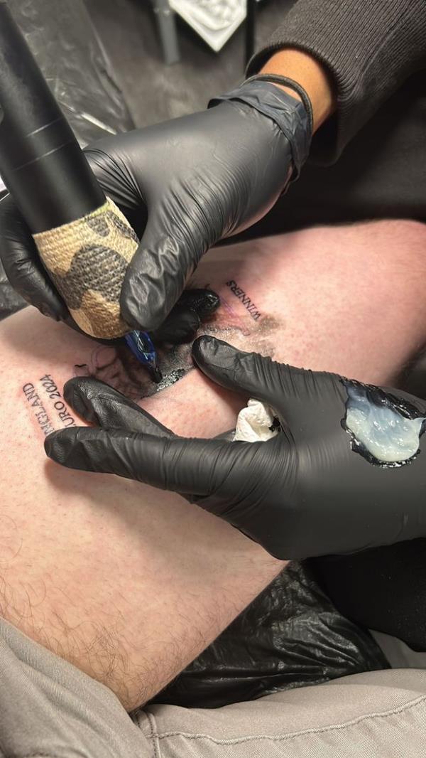 Tattoo artist tattoos a trophy and the words England Euro 2024 Winners on someone's leg
